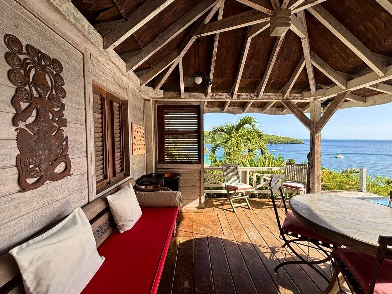 A wooden deck with a red cushioned bench, a table, and chairs.