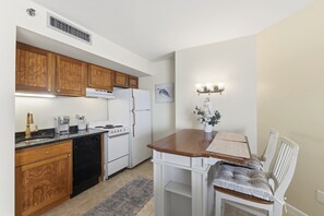 Eine Küche mit Holzschränken, einem weißen Kühlschrank, einer Kaffeemaschine und einem Essbereich mit einem weißen Stuhl und Tisch.
