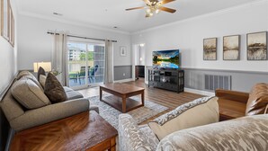 A living room with a sofa, coffee table, TV, and artwork on the wall. - Magnolia Pointe Magnolia Lake 4812-102 | Lakeview Myrtlewood Retreat Near Beach & Golf (Myrtle Beach)
