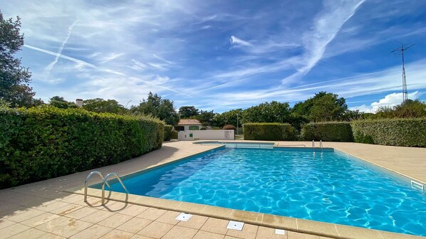 A rectangular swimming pool with clear blue water, surrounded by a tiled deck and bordered by neatly trimmed hedges.