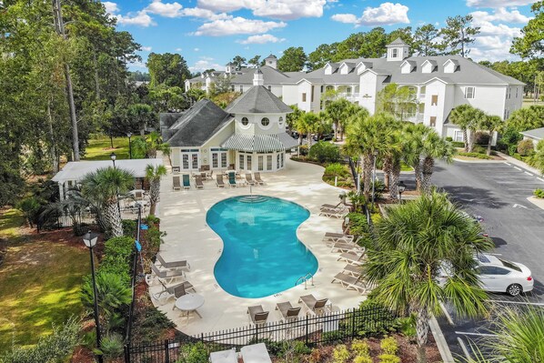 A resort with a swimming pool, lounge chairs, and a large building with a distinctive tower. - World Tour 1033-102 in River Oaks | World Tour Golf Retreat Near Beach & Dining (Myrtle Beach)
