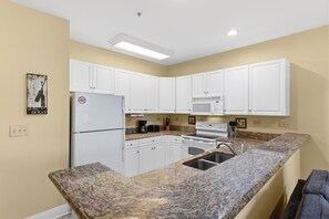 A kitchen with white cabinets, a granite countertop, a refrigerator, a microwave, and a stove. - World Tour 1033-102 in River Oaks | World Tour Golf Retreat Near Beach & Dining (Myrtle Beach)