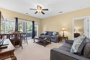 A living room with a ceiling fan, a sofa, a coffee table, and a dining area with chairs. - World Tour 1033-102 in River Oaks | World Tour Golf Retreat Near Beach & Dining (Myrtle Beach)