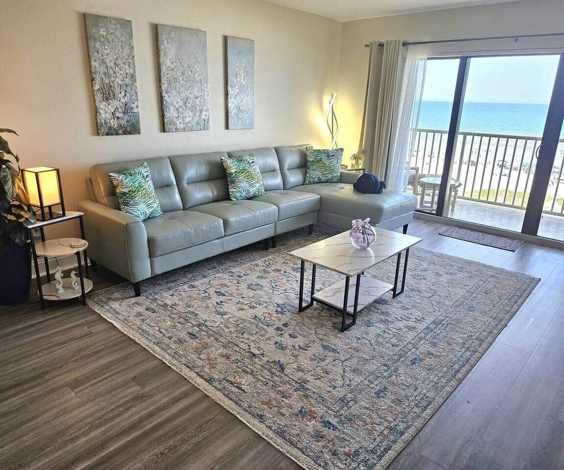 A living room with a sofa, a coffee table, and a view of the beach.