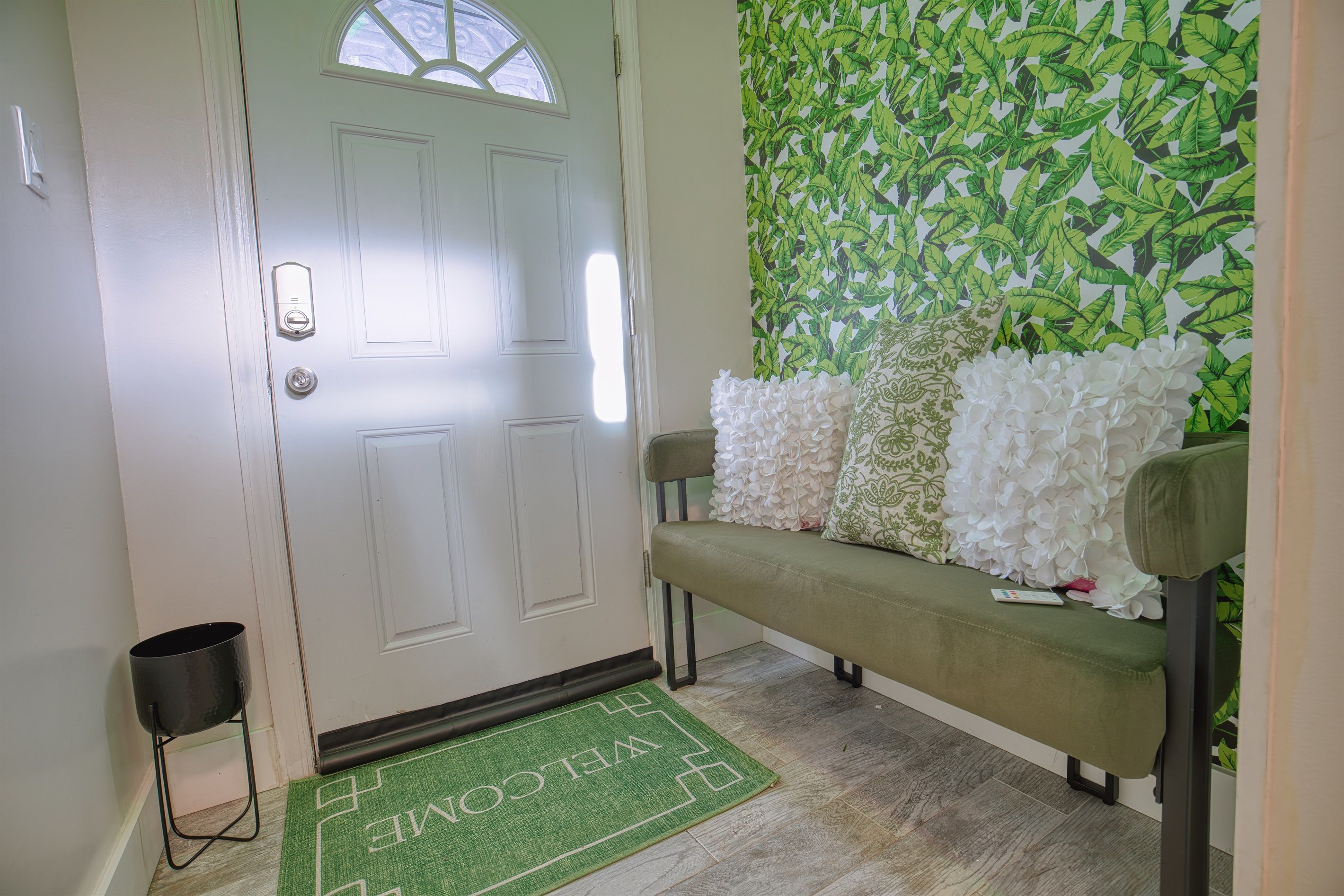 A door with a window, a bench with white and patterned cushions, and a green welcome mat.