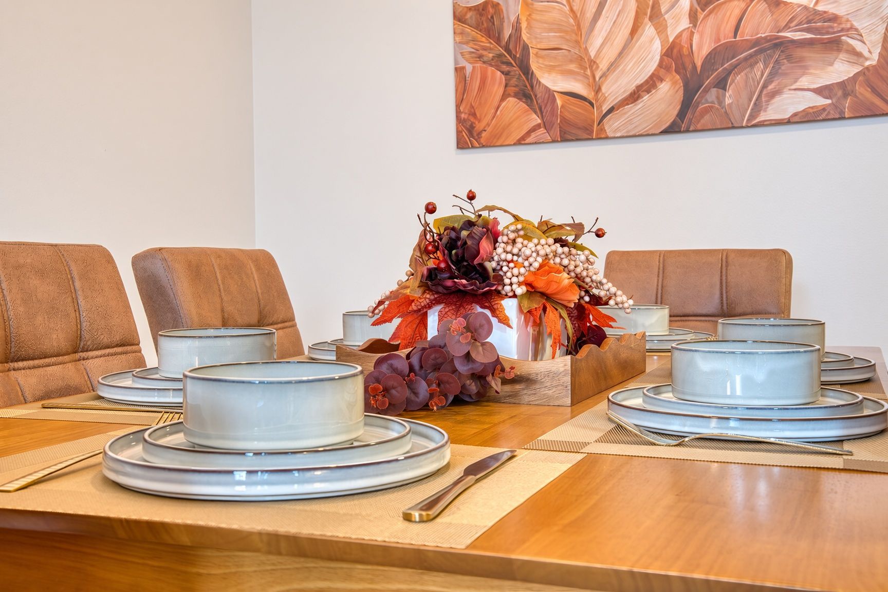 Une table à manger dressée avec des assiettes, des bols et un centre de table composé de fleurs et de raisins.