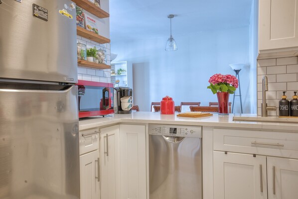 A modern kitchen with white cabinetry, a Bosch dishwasher, a red kettle, and a vase with pink flowers.