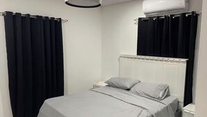 A bedroom with a bed, a nightstand, a white radiator, and black curtains.