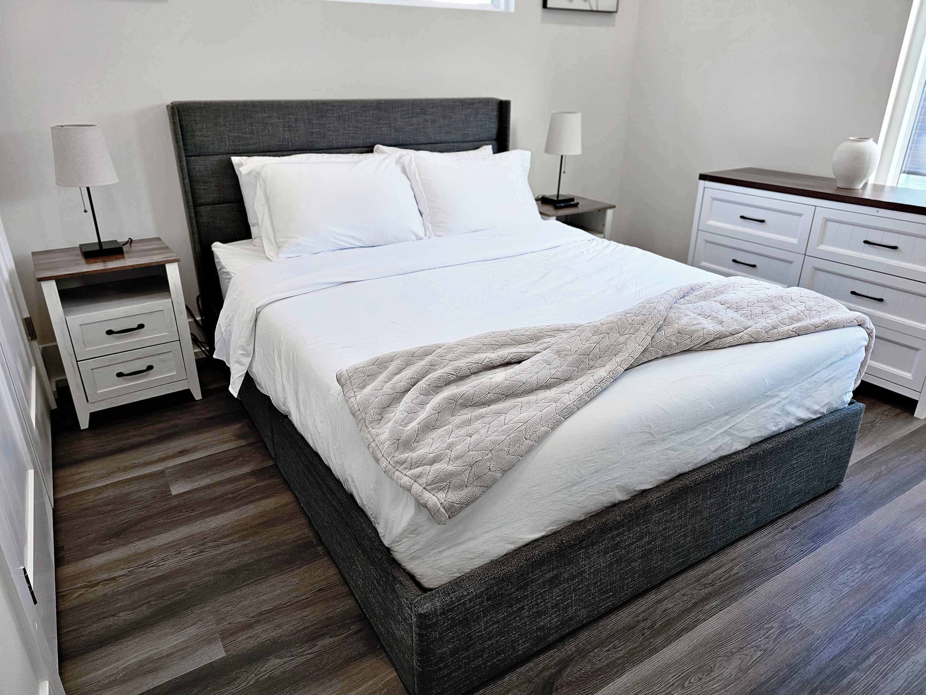 Ein modernes Schlafzimmer mit einem großen Bett, zwei Nachttischen, einem Beistelltisch und einer Kommode.