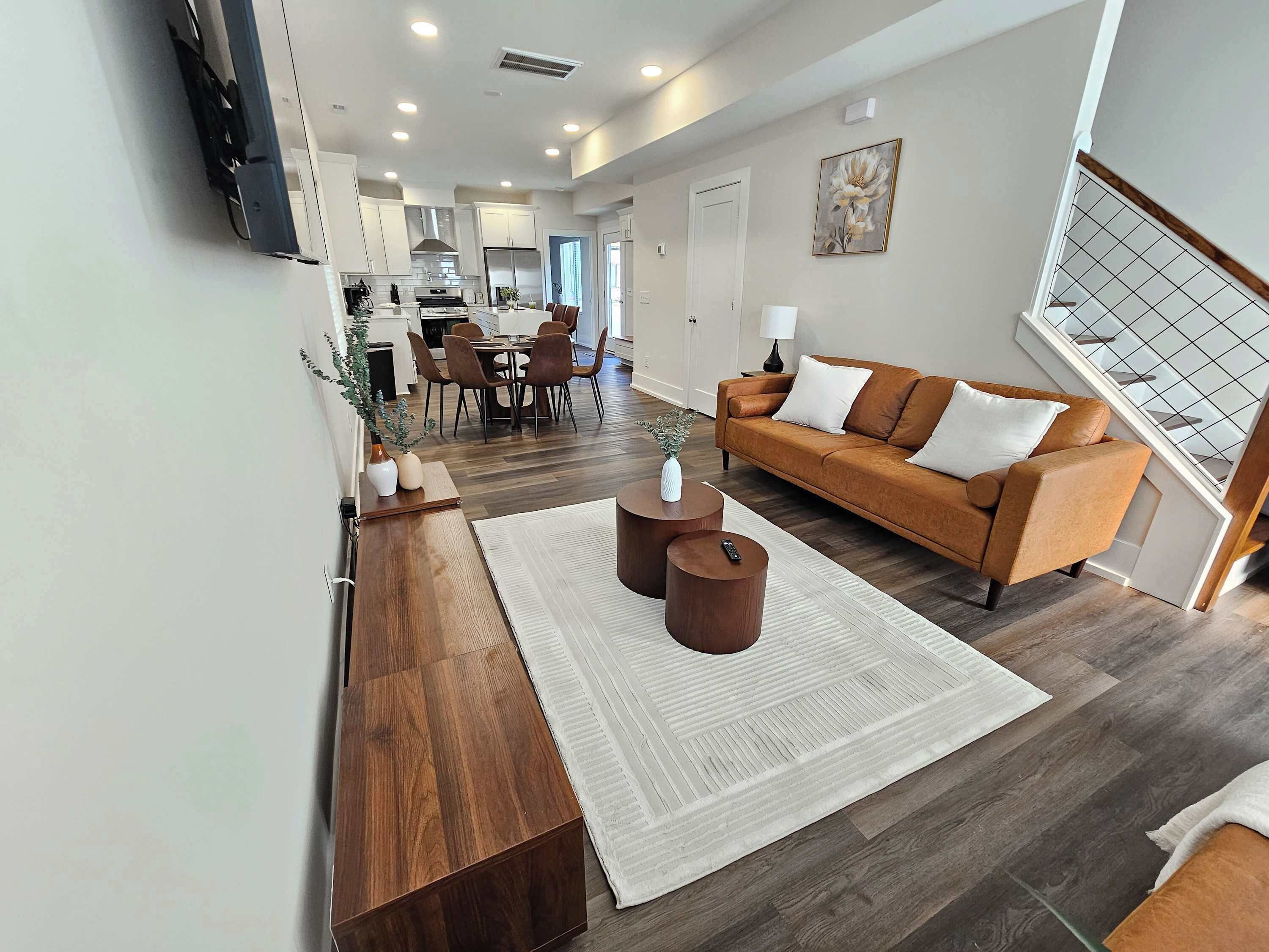 Ein modernes Wohnzimmer mit einem braunen Sofa, einem Holztisch und einem Essbereich mit Tisch und Stühlen.