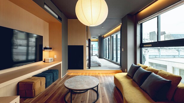 A modern interior with a flat-screen TV, a round table, a sofa with cushions, and large windows. - craft hotel antenna SHINJUKU KOENJI (Tokyo)