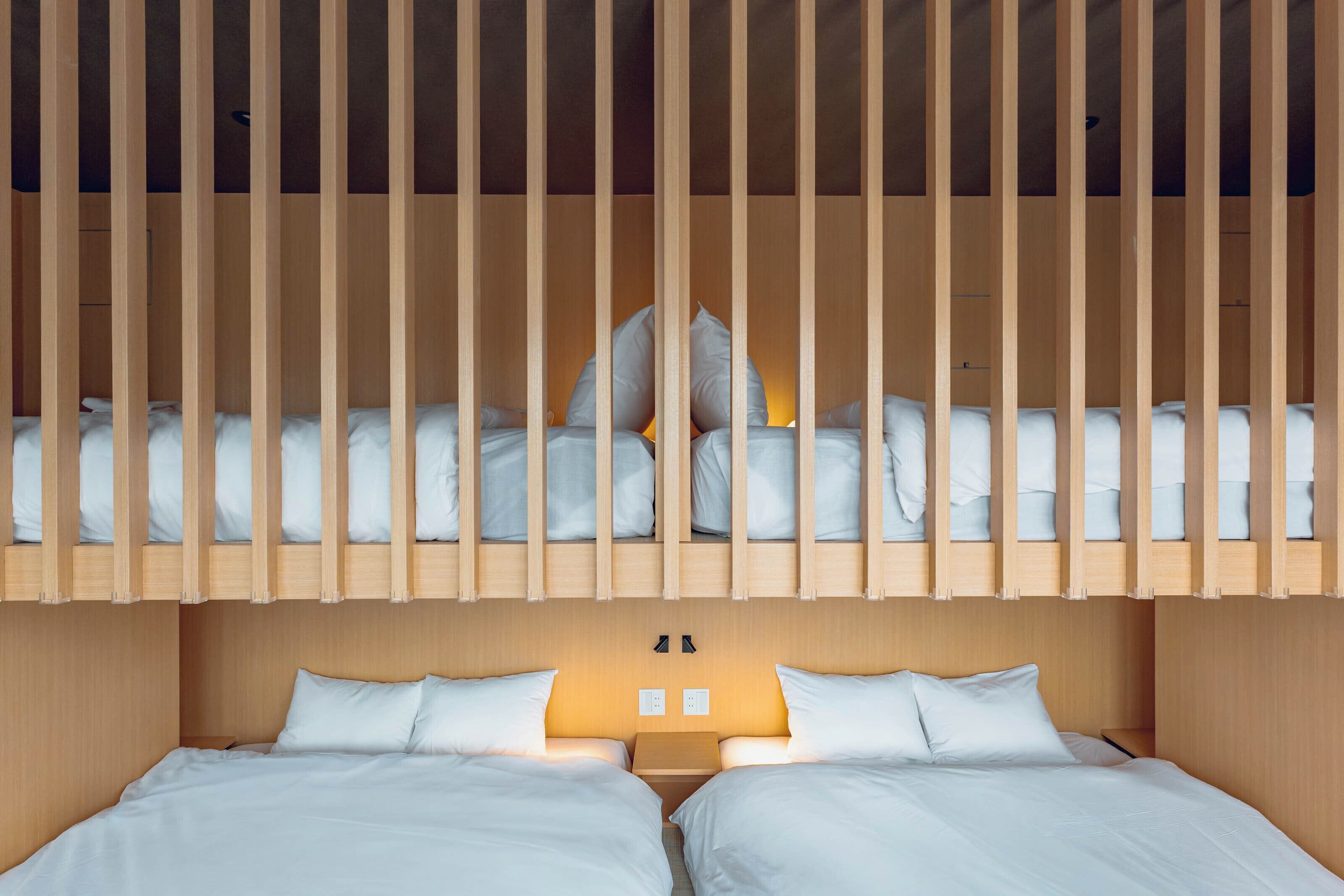 A room with two beds, wooden slats above, and a wall-mounted light fixture.