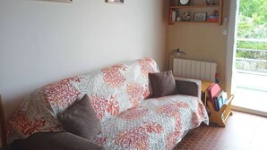 Ein Wohnzimmer mit einer Couch, einem Heizkörper, einem Fenster mit Aussicht und Wandschränken mit Büchern und Dekoration.