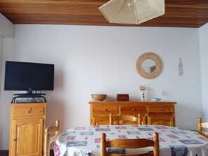 A bedroom with a TV, wooden furniture, a bed with a patterned bedspread, a woven wall hanging, and a wall-mounted mirror. - Les pieds dans l'eau - Saint Hilaire de Riez (SAINT HILAIRE DE RIEZ)