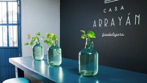 A bar area with three glass bottles containing plants on a blue counter, a stool, and a wall with 'CASA ARRAYÁN Guadalajara' signage. - Casa Arrayán | Downtown Guadalajara | Beautiful Colonial Home with Courtyard (Guadalajara)