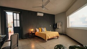 A bedroom with a bed, a desk, a chair, a ceiling fan, a window, and a door. - Casa Arrayán | Downtown Guadalajara | Beautiful Colonial Home with Courtyard (Guadalajara)