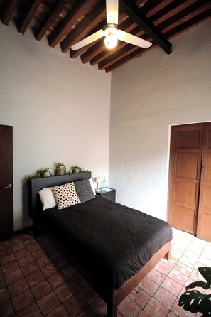 A bedroom with a bed, a ceiling fan, a wooden door, and a tiled floor. - Casa Arrayán | Downtown Guadalajara | Beautiful Colonial Home with Courtyard (Guadalajara)