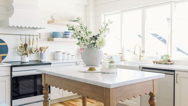 A modern kitchen with a wooden island, white cabinetry, and a large window providing natural light.
