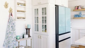 A kitchen with white cabinetry, a glass-fronted refrigerator, and shelves with jars and decorative items.