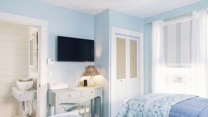A bedroom with a bed, a dresser, a television, and a window with curtains.