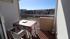 Un balcón con mesa y sillas, vistas a edificios de apartamentos y barandilla de metal.