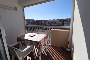 A balcony with a table and chairs, a view of apartment buildings, and a metal railing. - T2 cabin for 4 people, terrace, parking near the beach (LE GRAU DU ROI)