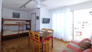Una habitación con literas, una mesa de comedor con sillas, un ventilador de techo, una televisión y un sofá.