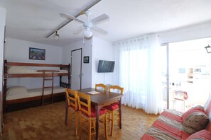 A room with a bunk bed, a dining table with chairs, a ceiling fan, a television, and a sofa. - T2 cabin for 4 people, terrace, parking near the beach (LE GRAU DU ROI)