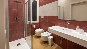 Ein modernes Badezimmer mit Duschkabine aus Glas, einem weißen Waschbecken, einem Bidet und einer Toilette.