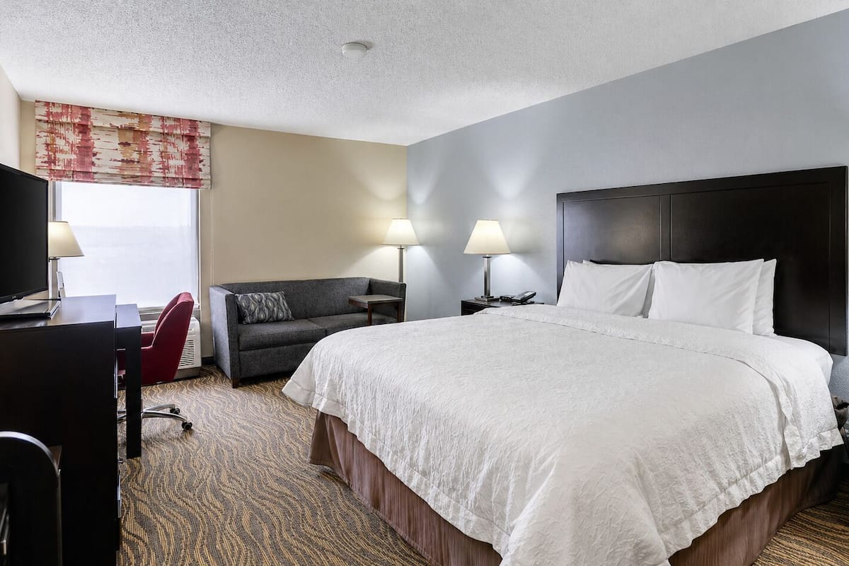 A hotel room with a large bed, a desk, a chair, and two bedside lamps.