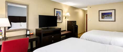 Ein Hotelzimmer mit zwei Betten, einem Fernseher, einem Schreibtisch mit Stuhl, einer Mikrowelle und gerahmten Bildern an den Wänden.