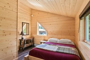 Une chambre dans un chalet en bois, avec un lit, un bureau, une fenêtre et un miroir.