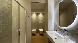 Uma casa de banho moderna com cabine de duche em vidro, um espelho grande e duas sanitas.