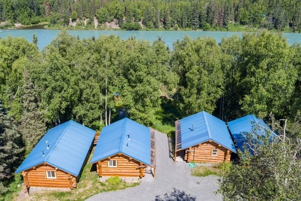 Eine Reihe von Blockhütten mit blauen Dächern, umgeben von dichtem Wald und einem See.