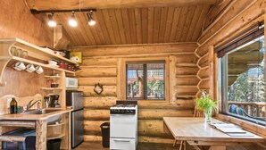A log cabin interior with a kitchen, dining area, and a window with a view.