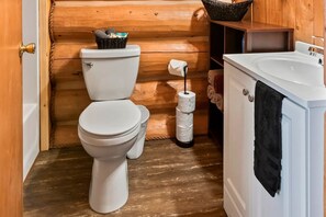 Ein kleines Badezimmer mit Toilette, einem Tablett mit Pflegeprodukten, einem Toilettenpapierhalter und einer Badewanne.