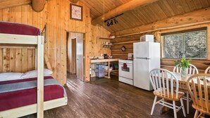 Interior de uma cabana de madeira com beliche, cozinha, mesa de jantar e cadeiras.