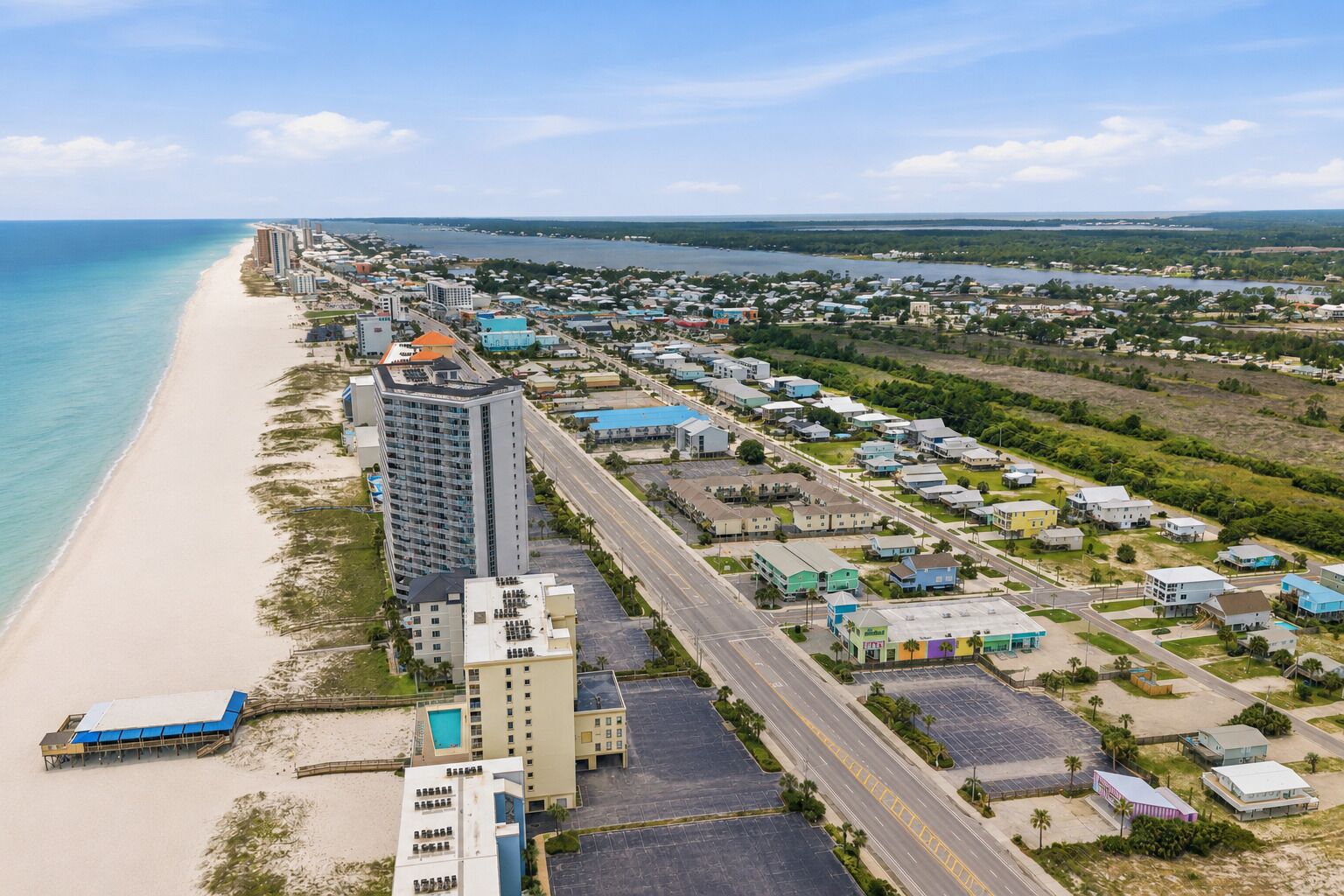 Vista aérea de una zona costera con una playa, un hotel grande de varios pisos y varios edificios más pequeños.