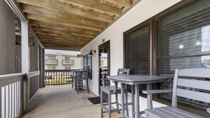 Ein möblierter Patio-Bereich mit Tischen und Bänken, Holzbalkendecke und Blick auf ein Gebäude im Hintergrund.