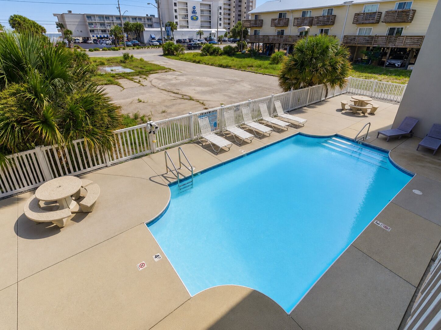 A swimming pool with lounge chairs and a table, surrounded by a white fence.