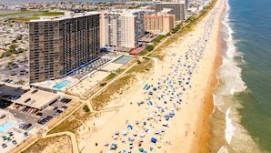 Un paisaje urbano costero con edificios altos, una playa arenosa con sombrillas y una vista despejada del océano.