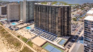 Un hotel moderno de gran altura con varias plantas, piscina, canchas de tenis y vista al agua.