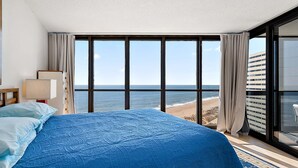 Habitación de hotel con una cama grande, vista a la playa y un balcón con puerta de vidrio.