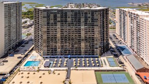 Un hotel de gran altura con varias plantas, piscina, canchas de tenis y zona de playa.