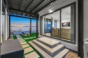 En moderne udendørs terrasse med udsigt til bjerge, en pool og et overdækket siddeområde.