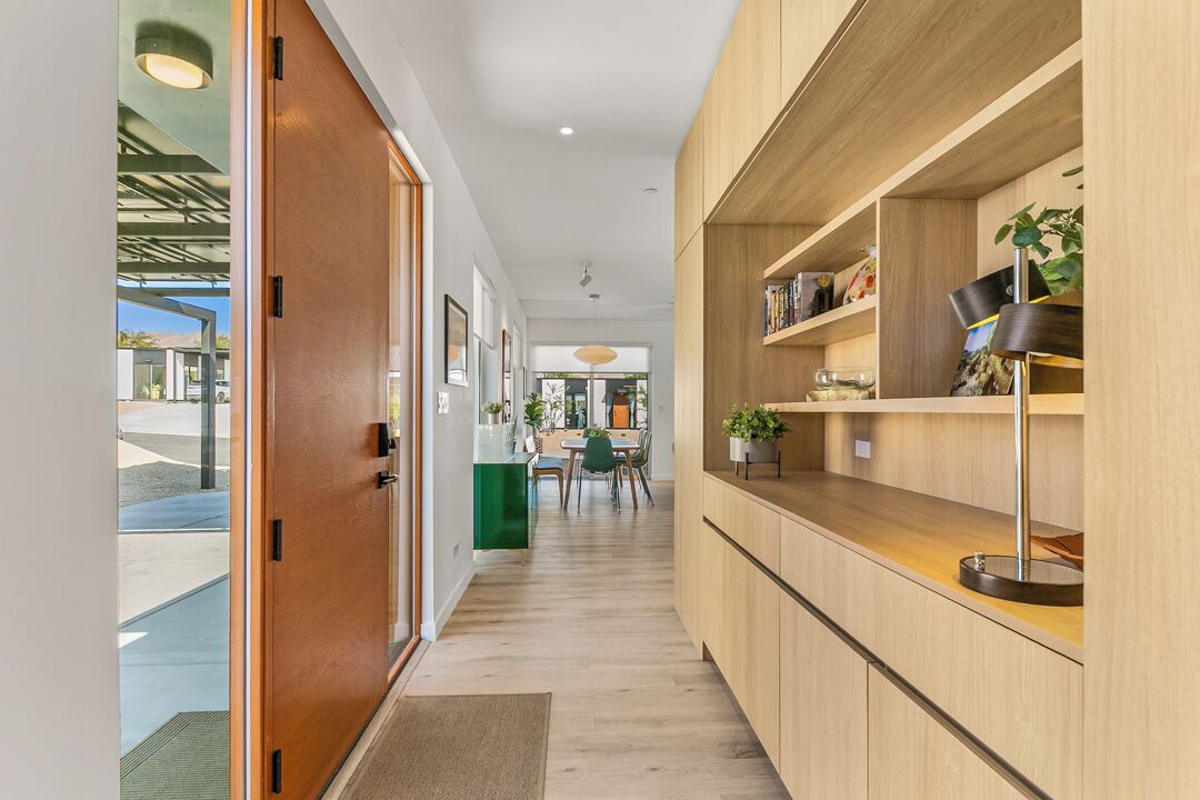 Un couloir avec des meubles de rangement en bois, un tapis vert et, au fond, un coin repas.