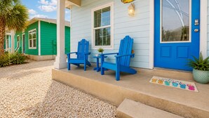 A house with a blue door, two blue Adirondack chairs, a small table, and a welcome mat. - SP3 Shared Pool, Pet Friendly, Parking for 3 (Port Aransas)