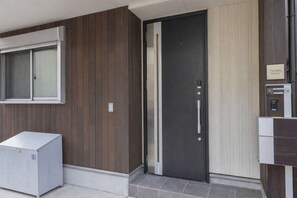 Una entrada moderna a un edificio con una puerta oscura, un ventanal y un pequeño letrero.