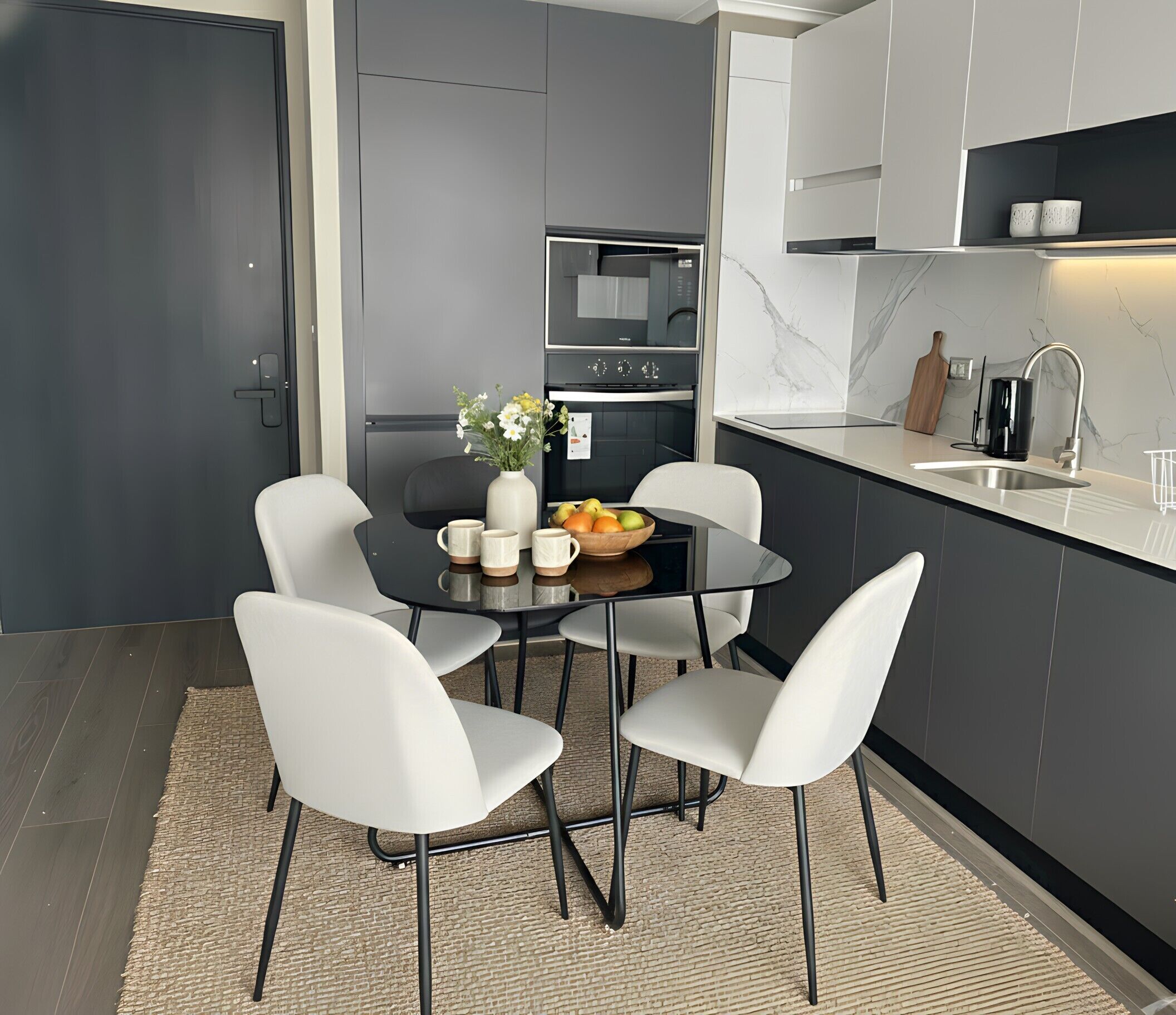 A modern kitchen with a dining table, chairs, a vase with flowers, and a fruit bowl.