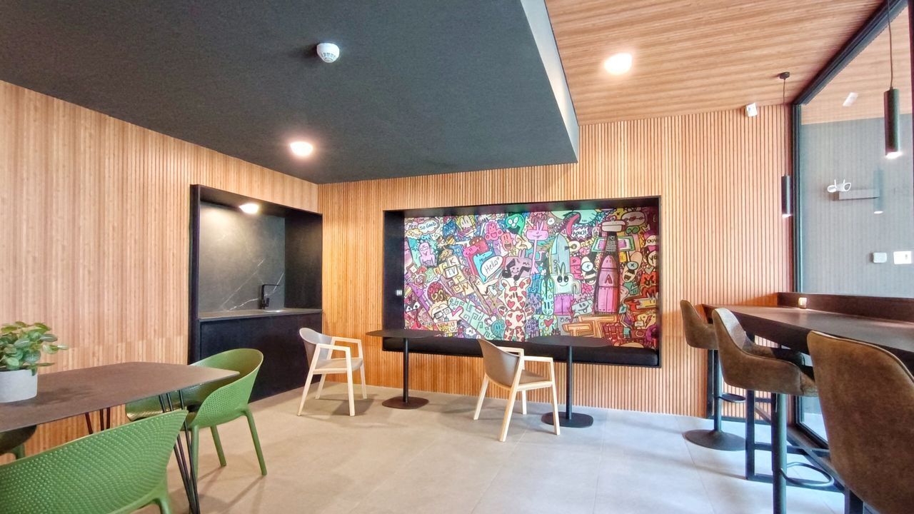 Un interior moderno con un gran mural colorido, paneles de madera en las paredes y una mezcla de sillas verdes y marrones alrededor de una mesa.